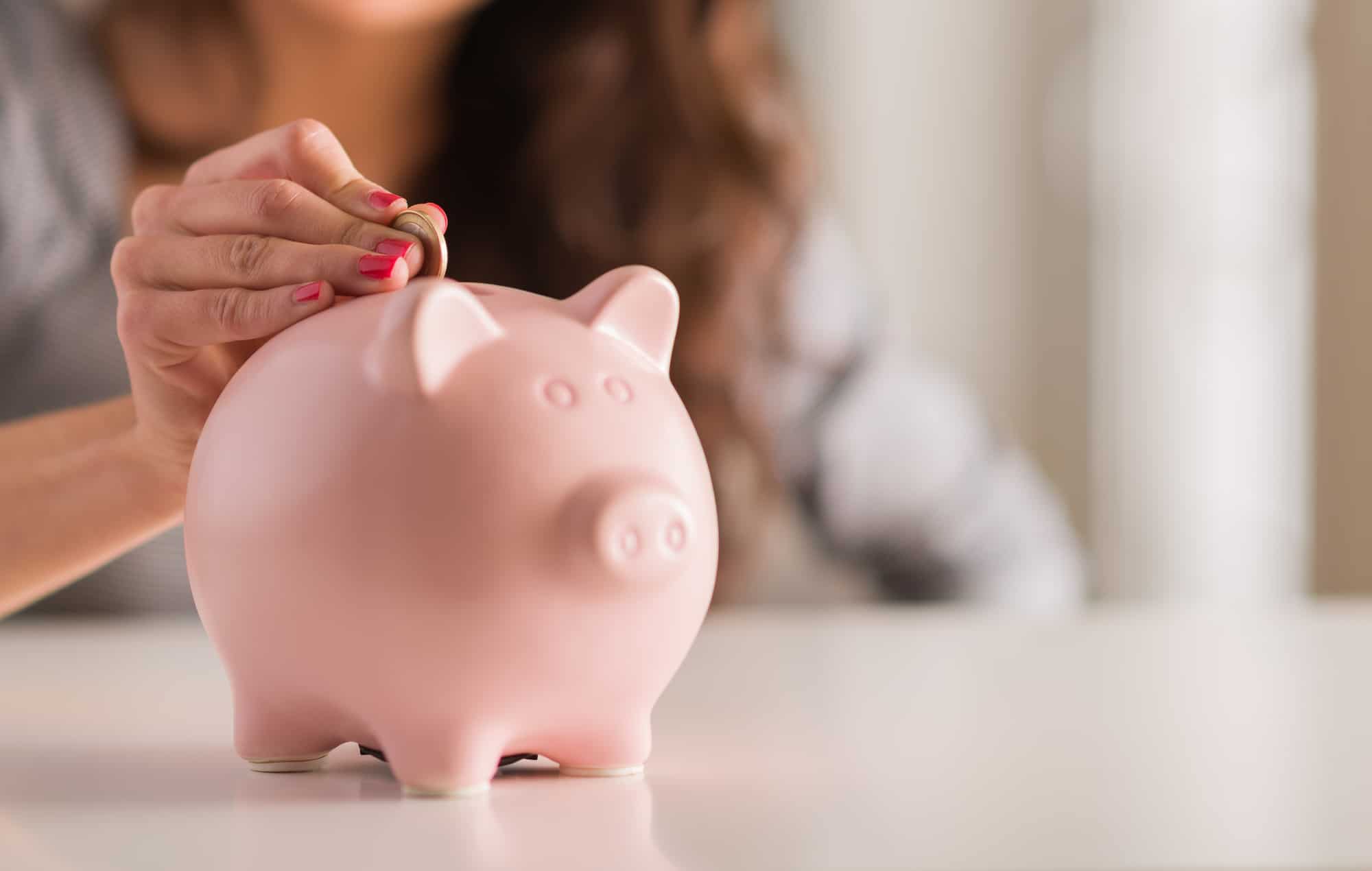 Woman Putting Coin In Piggy Bank