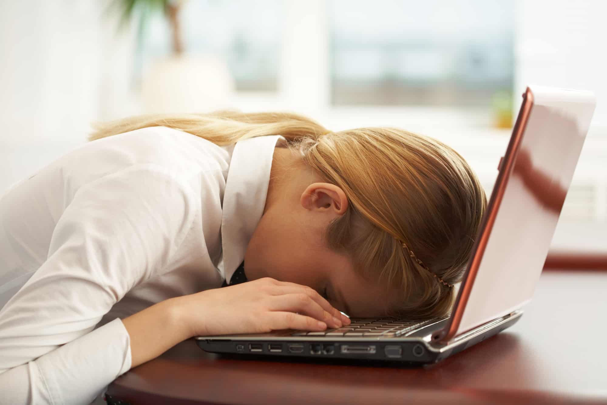 Exhausted woman with head on laptop