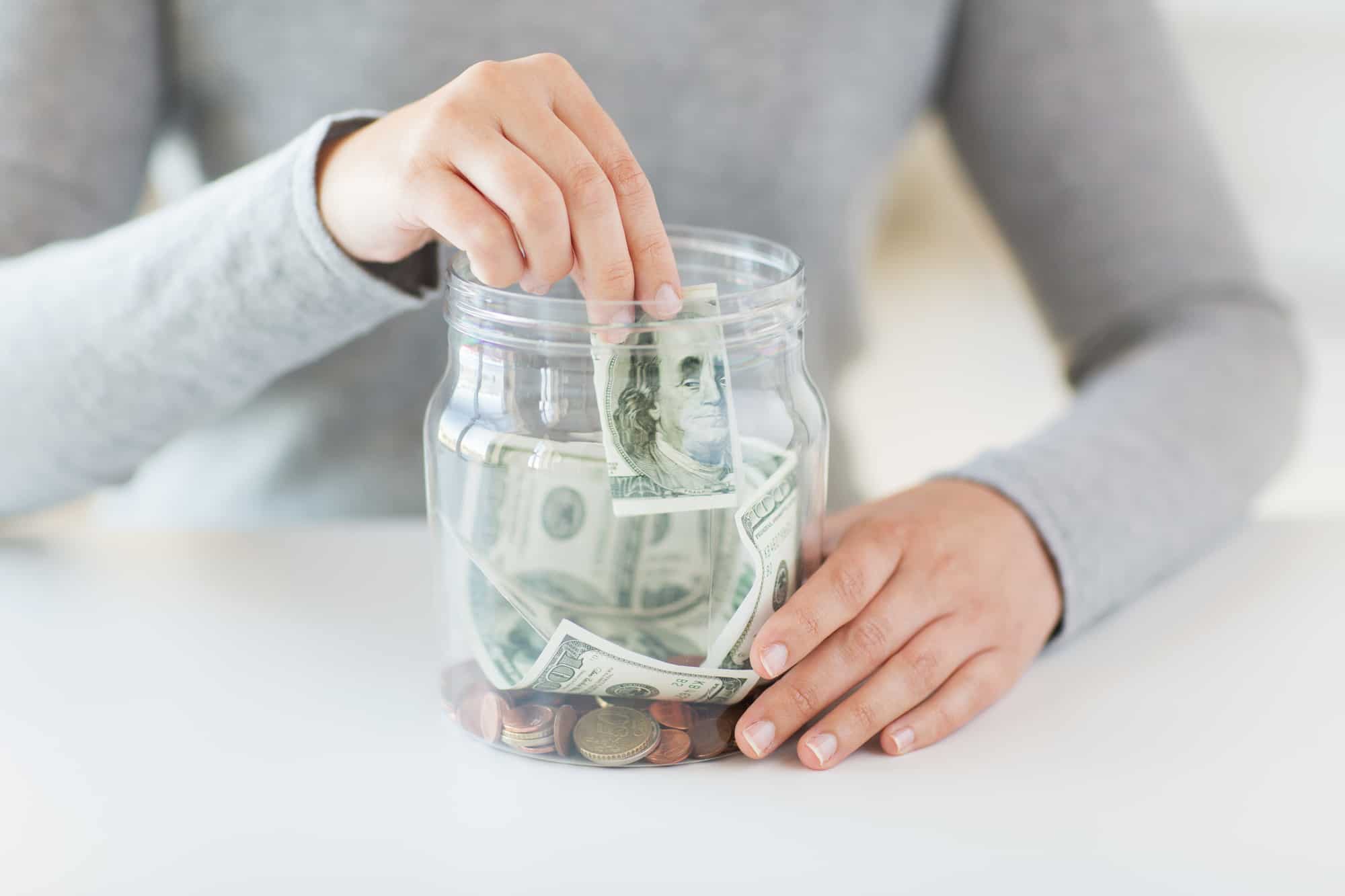 Close-up of woman hands and dollar money in jar