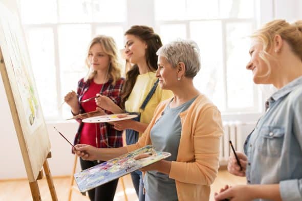 women with easel and palettes at art school