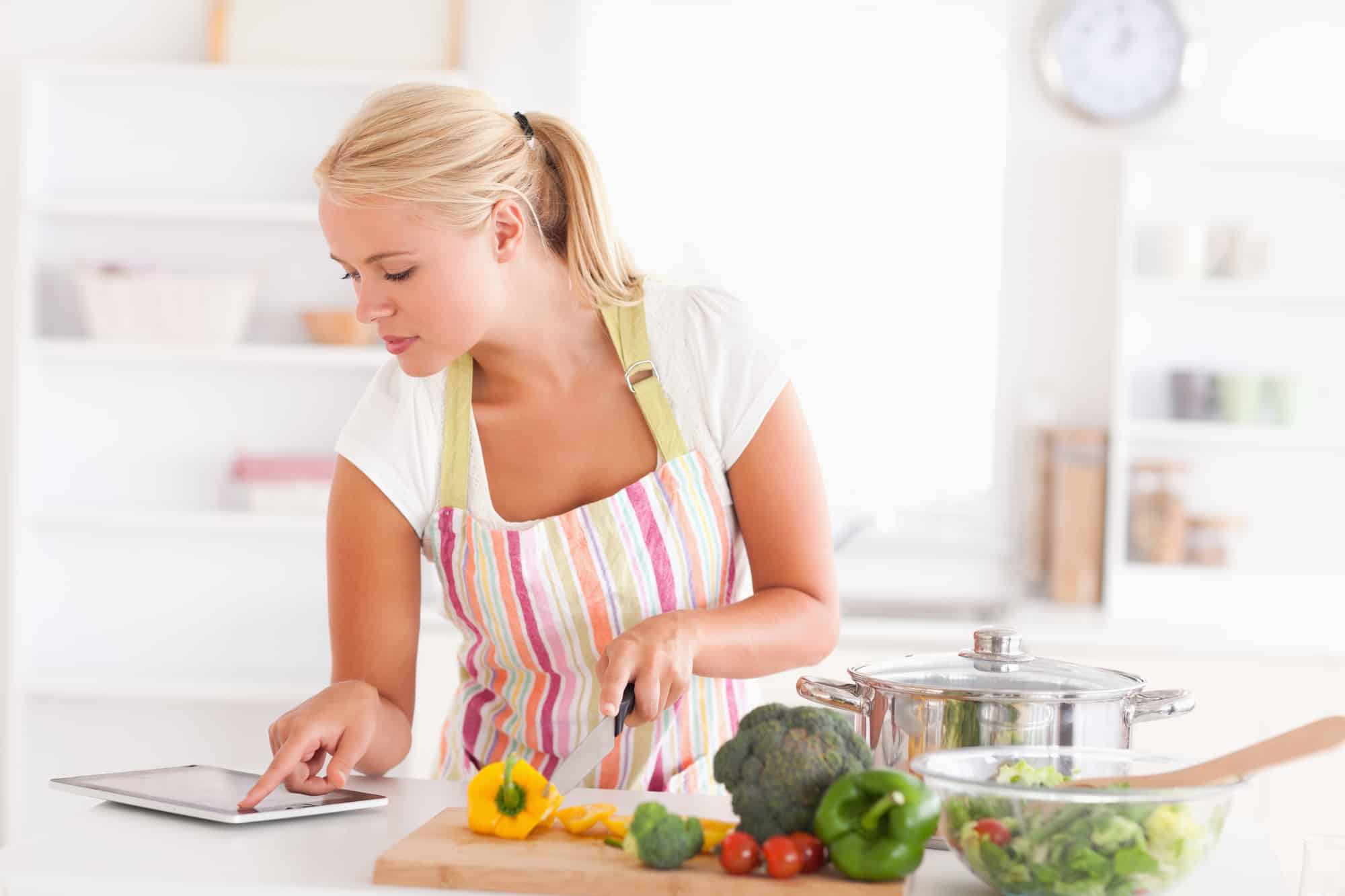 Woman cooking while looking at tablet