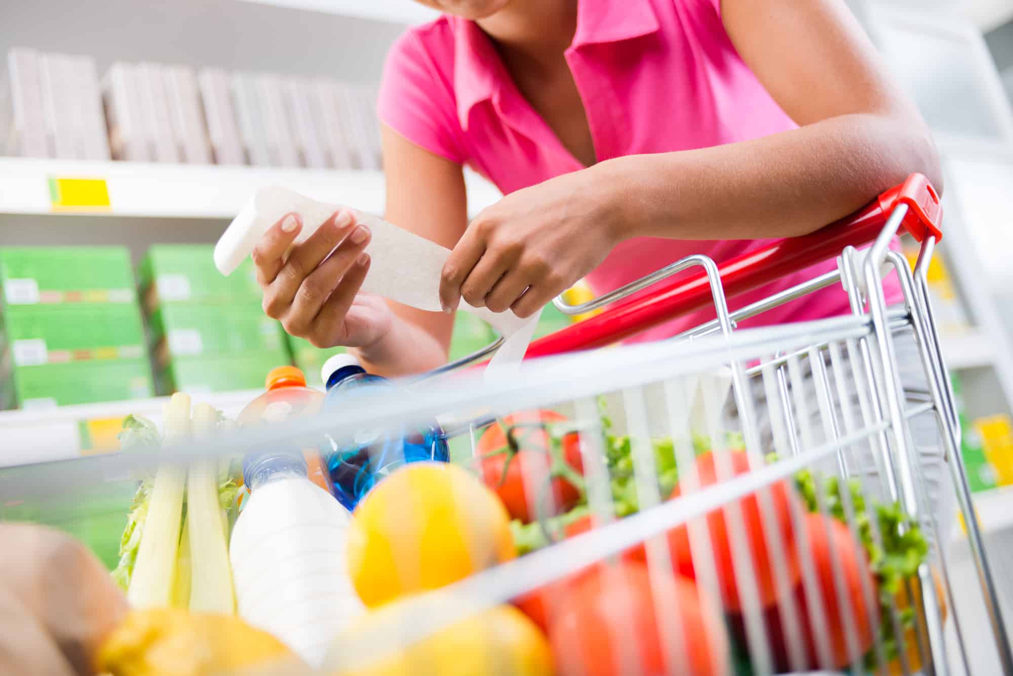 woman pushing supermarket shopping cart and holding receipt